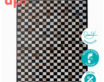 May include: Black and white checkered rug made from cowhide. The rug is handcrafted and has a reduced carbon footprint. The text "up!" is in the top left corner of the image.