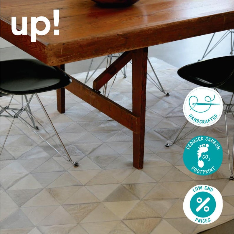 Pu&ograve; includere: Un tappeto geometrico bianco e grigio con un tavolo in legno e due sedie nere. Il tappeto ha tre etichette circolari blu turchese con il testo "Handcrafted", "Reduced Carbon Footprint" e "Low-End Prices".