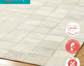 Può includere: Tappeto patchwork color crema con motivo geometrico. Il tappeto è composto da pezzi rettangolari cuciti insieme. Il tappeto è su un pavimento in legno. Il marchio "up! rfnry" è in alto a sinistra. Fatto a mano, a basso impatto ambientale.