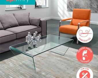 May include: A modern living room setup featuring a glass coffee table with a unique angled design. An orange armchair and gray sofa are visible. The image includes the text "up!rfnry" and circular icons with text.