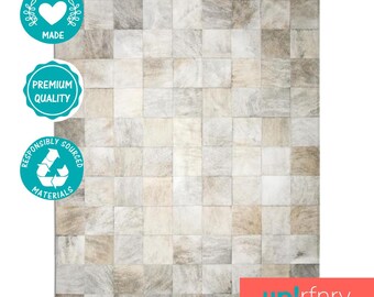 May include: A white and beige patchwork cowhide rug with a square pattern. The rug is ethically made with responsibly sourced materials. The rug is labeled as premium quality.