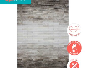 May include: A gray and white cowhide rug with a gradient pattern. The rug is made of hand-stitched leather pieces and has a reduced carbon footprint. The rug is available at low-end prices.