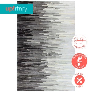 May include: A gray and white cowhide rug with a gradient pattern. The rug is made of hand-stitched leather pieces and has a reduced carbon footprint. The rug is handcrafted and has low-end prices.