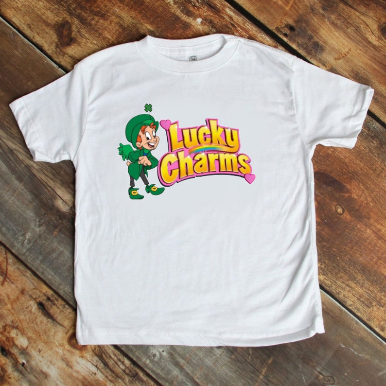 May include: White t-shirt with a green leprechaun and the words "Lucky Charms" in pink and yellow.