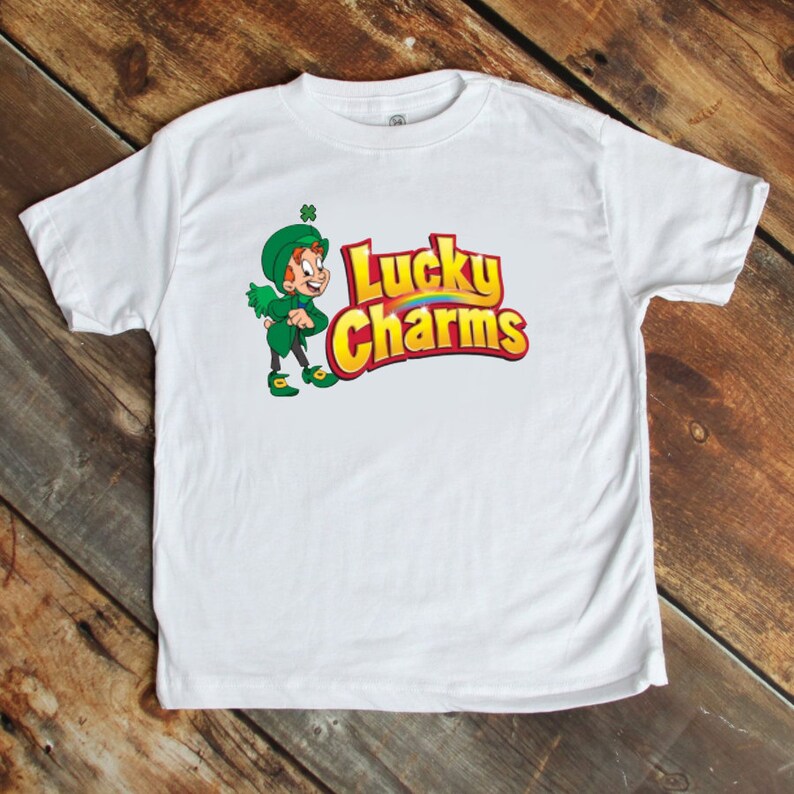 May include: White t-shirt with a cartoon leprechaun and the words "Lucky Charms" printed on the front.