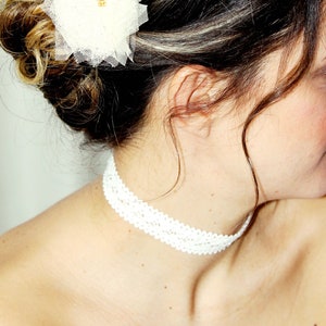 May include: A white tulle flower hair accessory with a gold centre. The flower is pinned to a woman's dark brown hair.