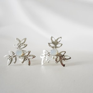 Könnte beinhalten: Ein Paar silberne Ohrringe mit einem zarten Blumenmuster und einem weißen Opal-Stein in der Mitte jedes Ohrrings.