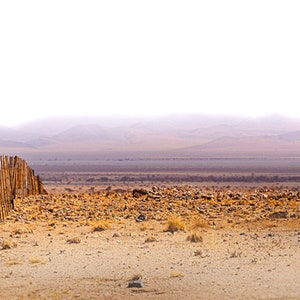 Könnte beinhalten: Ein Holzzaun erstreckt sich über eine Wüstenlandschaft mit einer nebeligen Bergkette im Hintergrund.
