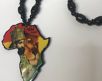 May include: Black beaded necklace with an Africa-shaped pendant. The pendant displays a portrait of a man and a lion, with the words "Lion of Judah". The necklace incorporates red, yellow, and green beads.