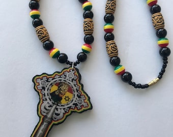 May include: A necklace with black, yellow, red, and green beads, and wooden barrel-shaped beads with etched patterns. The pendant features a portrait and a star. The necklace is a decorative item.
