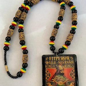 Può includere: Una collana di perline con un ciondolo raffigurante l'imperatore Haile Selassie. La collana ha perline nere, rosse, gialle e verdi. Il ciondolo rettangolare riporta la scritta "Emperor Haile Selassie King of Kings".