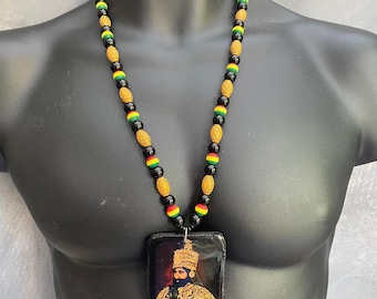 May include: A necklace with a pendant depicting a crowned figure. The necklace is made of black, gold, red, and green beads. The pendant is square and has a shiny surface. The beads are strung together.