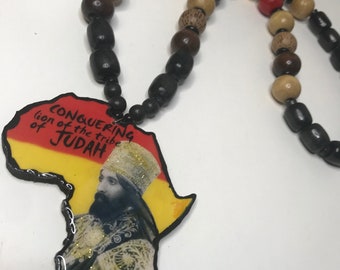 May include: A necklace with a pendant in the shape of Africa. The pendant has an image of a man and the text "Conquering lion of the tribe of Judah". The beads are in various colours and shapes.