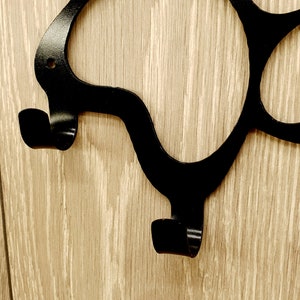 May include: Black metal wall hook with a unique, abstract design. The hook has two curved arms that extend out from the wall.
