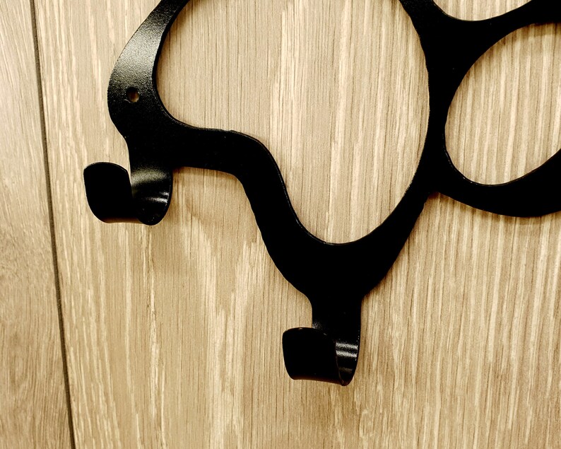 May include: Black metal wall hook with a unique, abstract design. The hook has two curved arms that extend out from the wall.