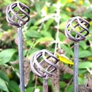 May include: Three metal garden stakes with decorative wire sphere tops. The spheres are made of twisted wire and are a dark brown colour.