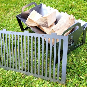 May include: A black metal fire pit with a grill grate. The fire pit is shaped like a dog's head and has a cutout of a flame. The grill grate is made of metal bars and is designed to fit inside the fire pit. The fire pit is sitting on a green grassy surface.