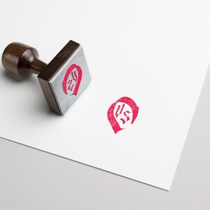 May include: A wooden stamp with a red ink impression of the letters "US" in a stylized font.