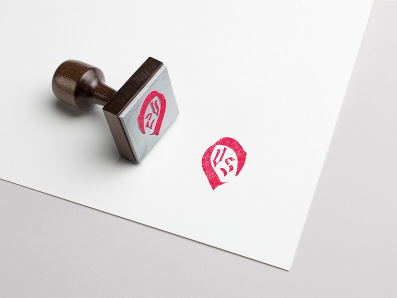 May include: A wooden stamp with a red ink impression of the letters "US" in a stylized font.