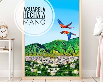 May include: A watercolor painting of a city landscape with two red and blue macaws flying over a green mountain. The painting is framed in a light wood frame and has the text "Acuarela hecha a mano" in a white circle.