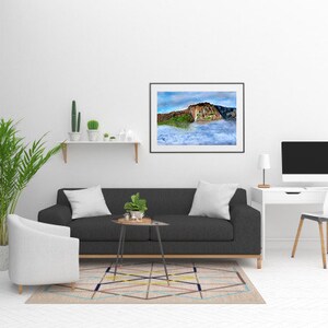 May include: A living room interior design with a black sofa, a white armchair, a white desk with a computer monitor, a white shelf with plants, and a framed landscape photograph of a mountain range with clouds.