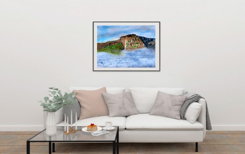 May include: A framed photograph of a large rock formation with a waterfall cascading down the side. The rock is surrounded by clouds and a blue sky.