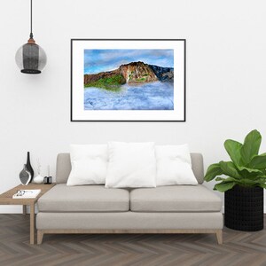 May include: A framed photograph of a mountain peak with clouds in the foreground. The mountain is brown and green with a waterfall cascading down the side. The clouds are white and fluffy.