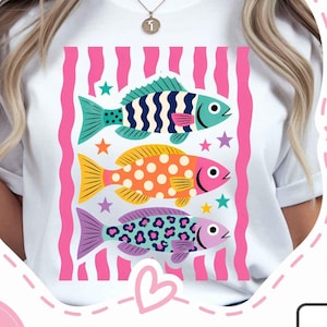 K&ouml;nnte beinhalten: Wei&szlig;es T-Shirt mit einem Design von drei bunten Fischen. Die Fische sind blau, gelb und lila, mit verschiedenen Mustern und Sternen. Der Hintergrund hat rosa und wei&szlig;e Streifen. Die Worte "INSTANT DOWNLOAD" stehen in einem rosa Kreis.