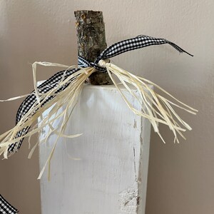 May include: White wooden block with a natural wood branch attached to the top. The branch is tied with black and white checkered ribbon and natural raffia.