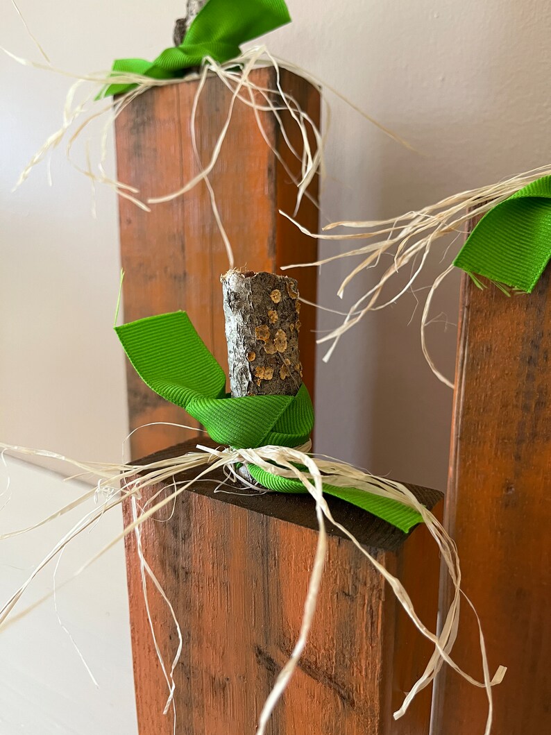 May include: Three wooden pumpkins decorated with green ribbon and natural twine. The pumpkins are stacked on top of each other.