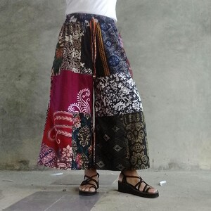 Può includere: Pantaloni palazzo patchwork a gamba larga in una varietà di fantasie e colori, tra cui bordeaux, nero e bianco. I pantaloni hanno una vita elasticizzata e sono indossati con sandali neri.