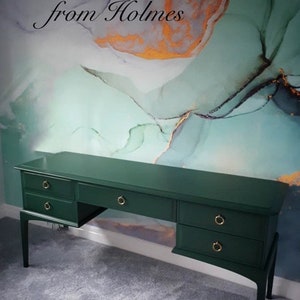 May include: A dark green desk with gold drawer handles. The desk has several drawers and a long, flat surface. The background features an abstract design in blue, green, and gold. The text "Homes from Holmes" is visible.