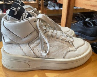 Könnte beinhalten: Off-White High-Top-Sneaker mit dicken Sohlen. Die Sneaker haben Schnürsenkel und ein Converse-Logo auf der Zunge. Die Schuhe sind aus Leder und haben ein Sternlogo an der Seite.