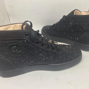 May include: A pair of black high-top sneakers with a sparkly finish. The sneakers have a black leather upper and a white rubber sole.