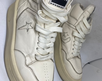 Könnte beinhalten: Ein Paar weiße Converse-Sneaker mit hohem Schaft und einer dicken weißen Sohle. Die Sneaker haben ein schwarzes Sternlogo an der Seite und ein schwarzes Etikett an der Seite, auf dem "Converse" und "TURBOWPK" steht.