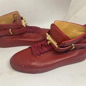 May include: A pair of red leather high-top sneakers with gold buckles and laces.