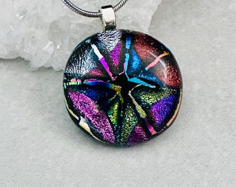 Könnte beinhalten: Eine silberne Kettenkette mit einem runden Anhänger mit einem farbenfrohen abstrakten Design in Blautönen, Lila, Rosa, Grün und Gold. Der Anhänger hat einen schwarzen Hintergrund und einen silbernen Rand.