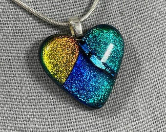 May include: A silver chain necklace with a heart-shaped pendant made of iridescent glass. The pendant is divided into three sections, each with a different color: yellow, blue, and green. The glass has a sparkly finish.