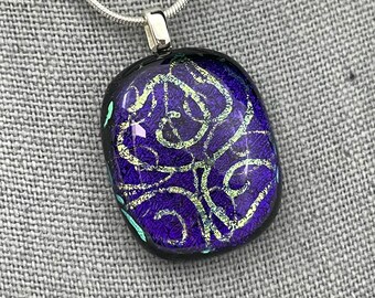 Könnte beinhalten: Eine silberne Kettenkette mit einem violetten und goldenen Glasanhänger. Der Anhänger hat ein wirbelndes Muster und einen schwarzen Rand.