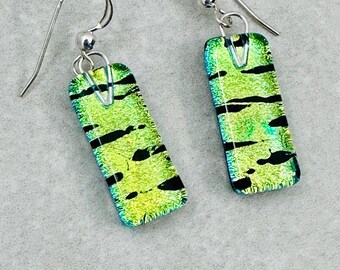 Könnte beinhalten: Ein Paar rechteckige Ohrringe mit einem dichroitischen Glasdesign. Die Ohrringe haben eine leuchtende grün-gelbe Farbe mit schwarzen Streifen und Akzenten. Die Ohrhaken sind silberfarben.