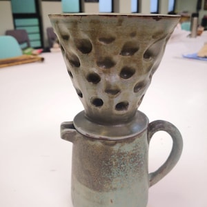 Peut inclure: Une théière en céramique avec un glaçage vert texturé. La théière a un filtre amovible et poreux avec un glaçage brun. Le filtre est conçu pour infuser du café ou du thé.