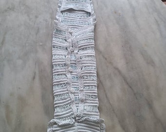 May include: A white crocheted baby garment with a button fastening and a frilled hem.