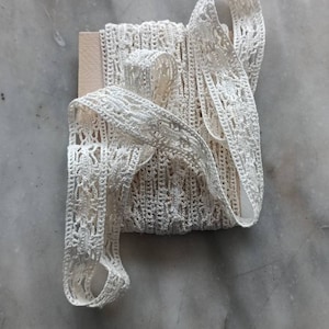 May include: A spool of white crocheted lace trim. The lace is delicate and intricate, with a floral pattern. The trim is perfect for adding a touch of elegance to any project.