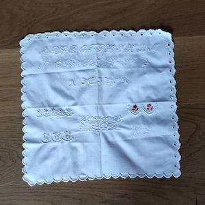 May include: White cotton handkerchief with embroidered alphabet, a floral design, and the text "A.J.E.L.I.C.H."
