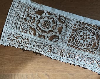 May include: A delicate white lace trim with intricate floral and geometric patterns. The lace is hand-stitched and features a delicate, scalloped edge.