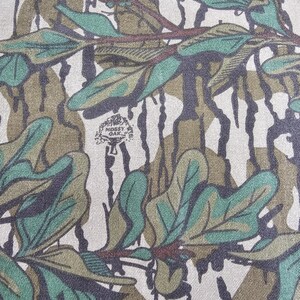 May include: Camouflage fabric with a green, brown and white pattern. The fabric features a repeating design of leaves and branches. The fabric is made from a soft, durable material.