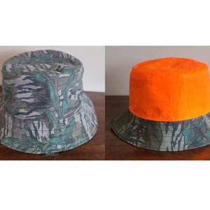 May include: Two bucket hats, one with a camouflage pattern and the other with a bright orange top and a camouflage bottom.