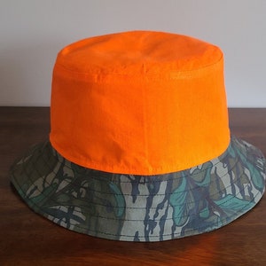 May include: A bright orange and camouflage bucket hat. The top of the hat is solid orange, and the brim is a camouflage pattern.