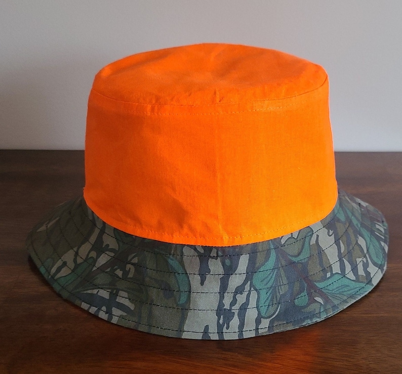 May include: A bright orange and camouflage bucket hat. The top of the hat is solid orange, and the brim is a camouflage pattern.