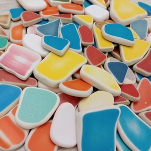 May include: A collection of colorful, irregularly shaped ceramic pieces. The pieces feature a variety of colors, including white, yellow, blue, orange, and red. The shapes vary from rounded rectangles to triangles, with a white border.